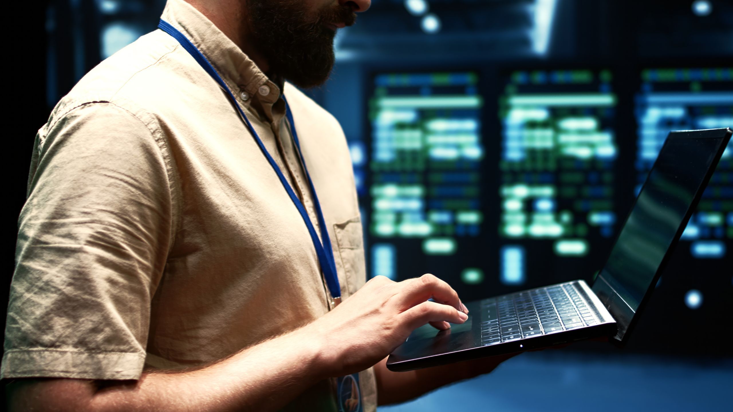 IT professional working on a laptop in a data center, with blurred server racks and network equipment in the background. IT professional working on a laptop in a data center, with blurred server racks and network equipment in the background.
